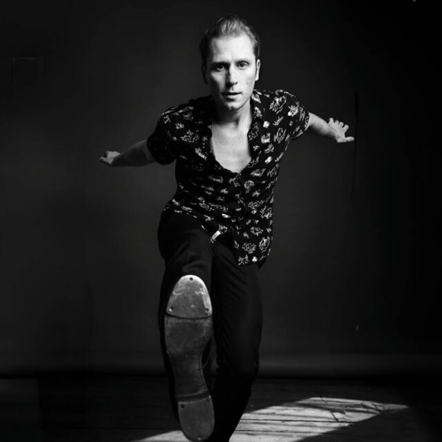 Black and white photo of tap dancer Tommy J Egan kicking his right foot forward