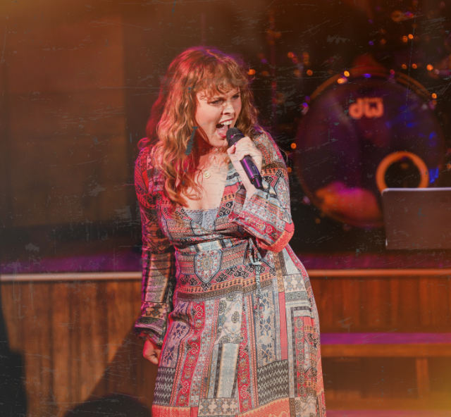 Woman on stage singing into a hand held microphone