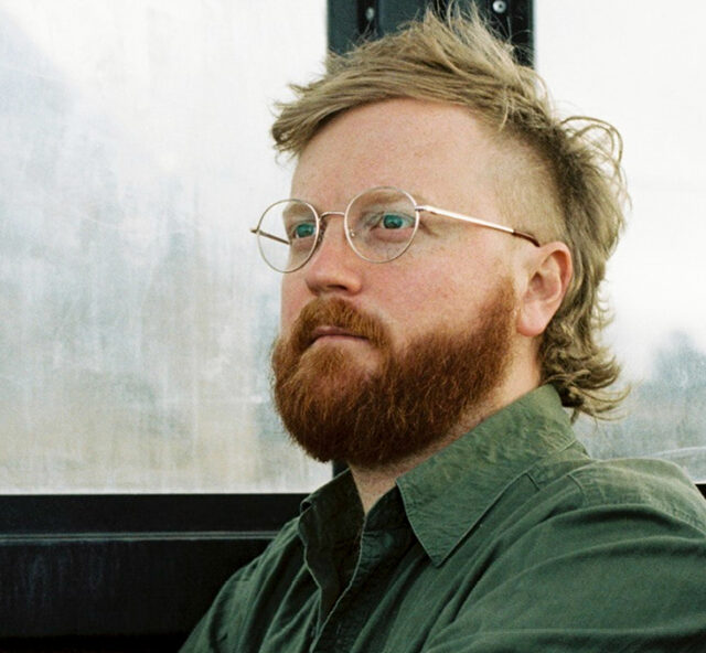 Head shot of James Bowers wearing a green shirt and a pair of glasses