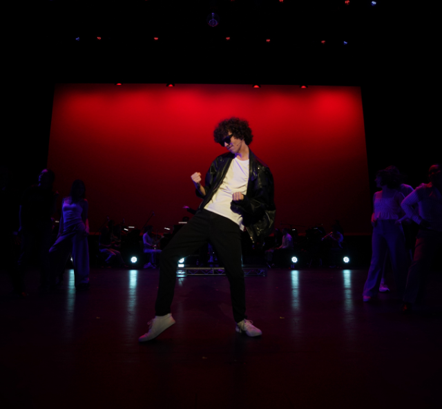 Solo dancer on stage in a white t-shirt and black pants and jacket