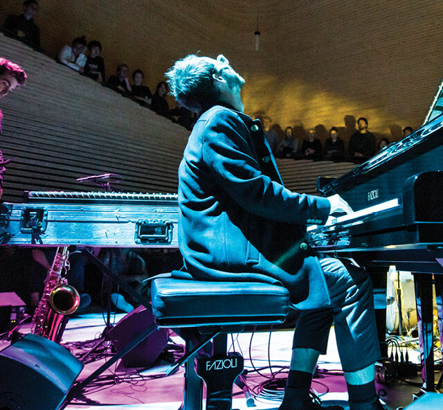 Pianist sitting at a grand piano playing on a concert hall stage