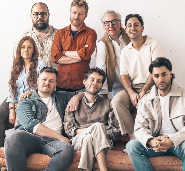 Eight cast members of The Last Sunday in June siting on and behind a couch in casual clothes
