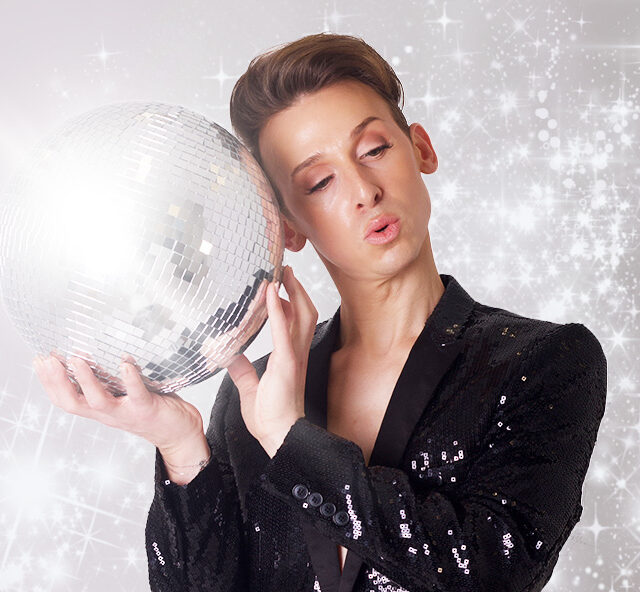 Artist Justin Clausen holding a small mirror ball up to his head and wearing a black sequined jacket