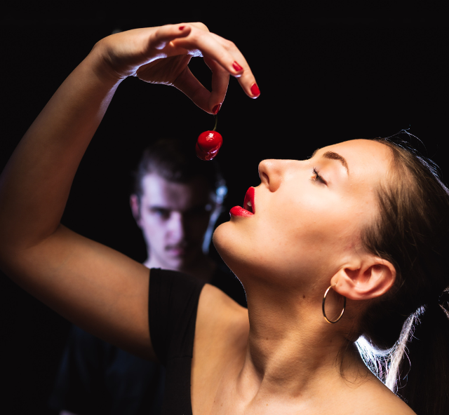 Side on profile of a woman dropping a red cherry slowly into her mouth