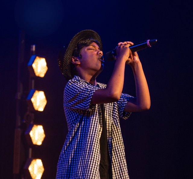 Singer singing into a stand microphone wearing a short sleeved shirt