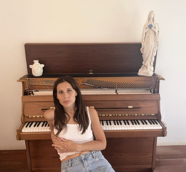 Singer Hannah Joy sitting on a stool leaning back on an upright piano