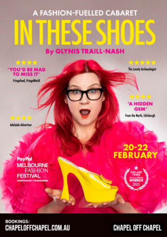 Artist Glynis Trail-Nash with red hair and a red fluffy cap holding a yellow shoe with a look of surprise on her face