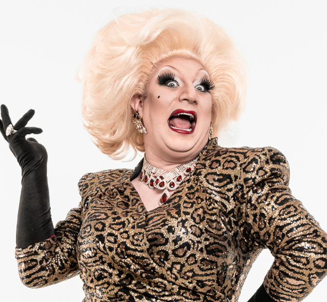 Artist Myra DuBois in a platinum blonde wig, wearing black gloves and a leopard skin print dress