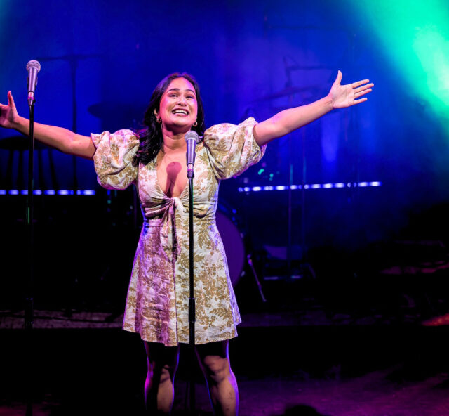 Singer in a skirt with arms outstretched singing