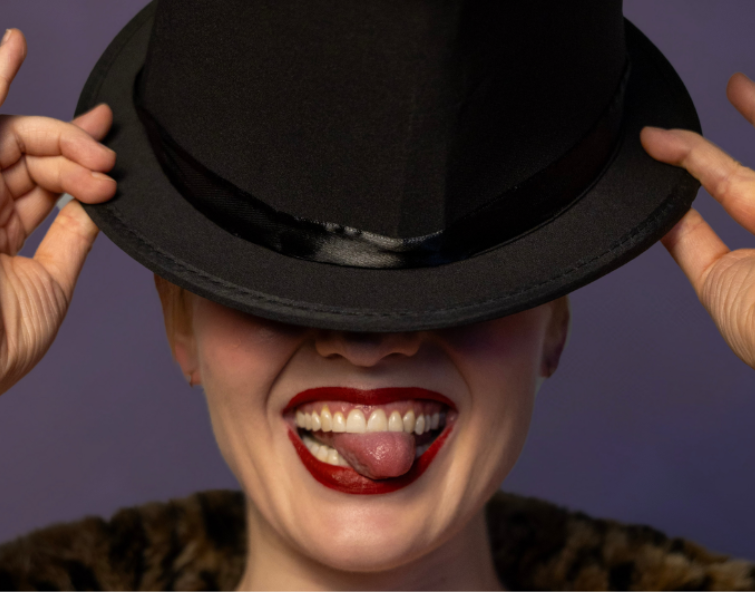 Face shot of a person poking their tongue out while tilting a top hat over their face